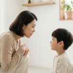 16:10 aspect ratio, realistic photo style, Korean parent calmly talking to a preschool child at eye level in a bright living room, warm and reassuring atmosphere, positive discipline concept, no anger, soft natural light, clean white background, ample margins, professional parenting guide thumbnail, all people appear Korean